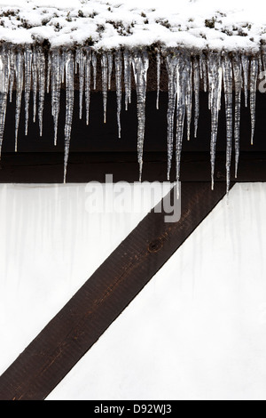 Schnee und eine Reihe von Eiszapfen hängen von der Traufe eines Gebäudes Stockfoto