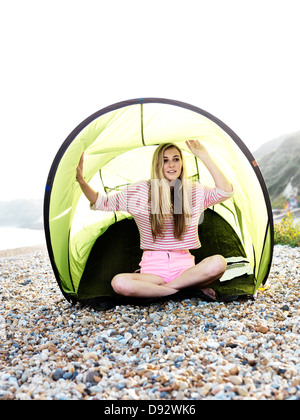 Eine junge Frau sitzt in einem Strandzelt an einem steinigen Strand Stockfoto