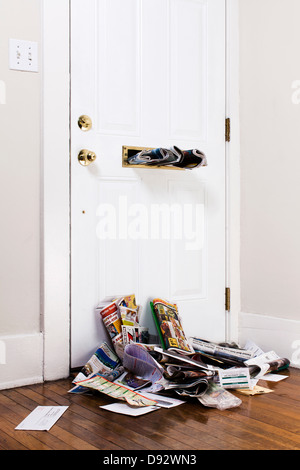 Zeitungen in einen Mailslot über einen Haufen von e-Mails innerhalb einer Haustür stecken Stockfoto