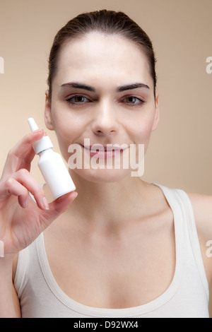 Eine lächelnde junge Frau mit einer Flasche Nasenspray Stockfoto