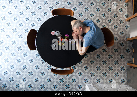 Eine müde Mann mit seinem Kopf ruht auf seinen Armen sitzen an einem Tisch direkt oberhalb Stockfoto