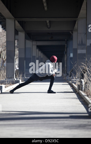 Ein junger Mann eine Dehnung Longe auf einem Bürgersteig unter einer Brücke zu tun Stockfoto