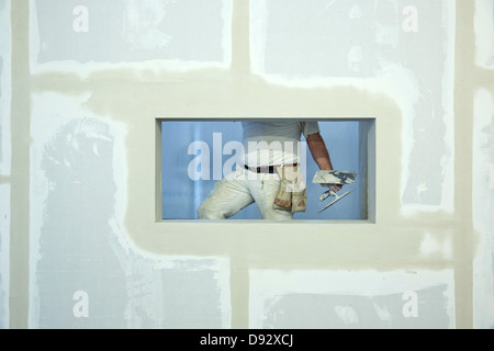 Mit einer Kelle, gesehen durch Fensteröffnung in einer neu errichteten Mauer Anstreicher Stockfoto