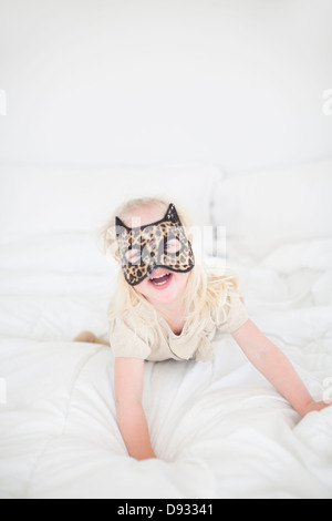 Mädchen mit Katzenmaske auf Bett liegend Stockfoto
