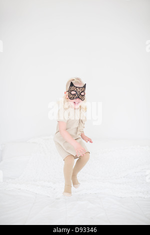 Mädchen mit Katzenmaske springen auf Bett Stockfoto