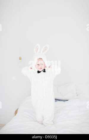 Mädchen tragen Kaninchen Kostüm stehen auf Bett Stockfoto