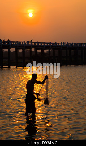 Ein Fischer wirft sein Netz unter U KLANGKUNST Brücke auf Taungthaman See bei Sonnenaufgang - AMARAPURA, MYANMAR Stockfoto