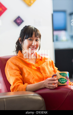 Asiatische Frau, die Tasse Kaffee im Sessel Stockfoto