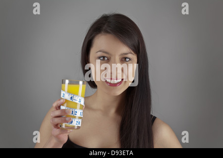 Eine attraktive junge Frau trinken Orangensaft aus einem Glas mit einem Maßband um Glas gewickelt Stockfoto