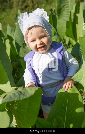 Lächelndes hübsches kleines Kind Mädchen in Blättern der Klette im park Stockfoto