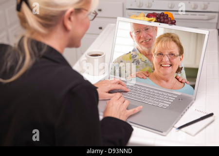 Frau In der Küche mit Laptop - Online-Chat mit älteres Paar oder Eltern auf dem Bildschirm. Stockfoto