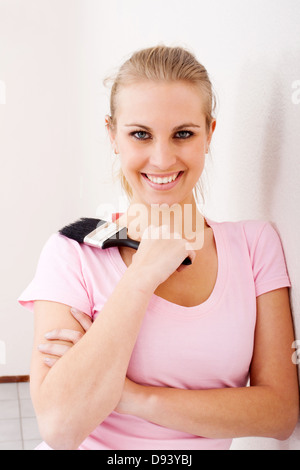 hübsche junge Frau mit einem Pinsel gegen Wand Stockfoto
