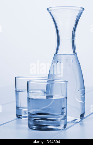 Wasserkaraffe und zwei Gläser - eine Karaffe Wasser auf einem Tisch mit zwei Gläsern, blau getönt. Stockfoto