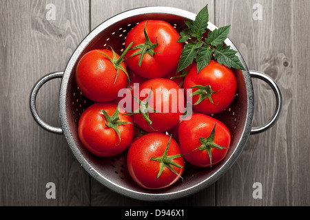 Frische Tomaten mit grünen Blatt und Wassertropfen in Sieb auf hölzernen Hintergrund. Ansicht von oben Stockfoto