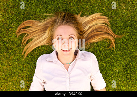 Junge Frau, die auf Rasen Hintergrund auf der Suche nach oben liegend Stockfoto