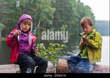 Jungen und Mädchen sitzen auf Protokolle per See, Mädchen bläst Seifenblasen Stockfoto