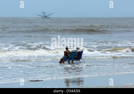 Älteres Ehepaar sitzen auf Stühlen in der Brandung am Strand, Hunting Island, South Carolina Stockfoto