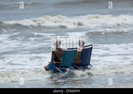 Älteres Ehepaar sitzen auf Stühlen in der Brandung am Strand, Hunting Island, South Carolina Stockfoto