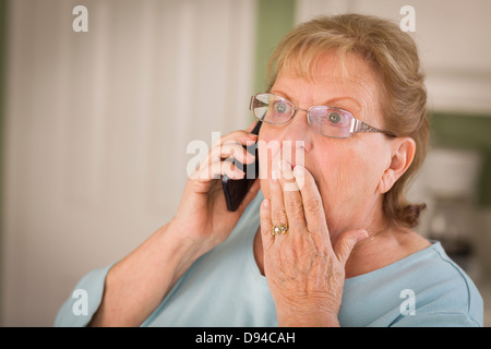 Schockiert Senior Erwachsene Frau auf Handy mit der Hand über den Mund in Küche. Stockfoto