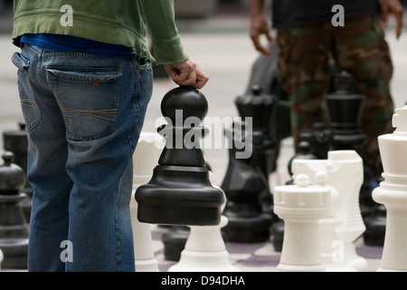 Ein Mann geht seinen riesigen Bauern in eine Partie Schach auf der Straße Stockfoto