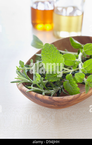 Frische Kräuter in einer Schüssel und Flaschen Öl für Aromatherapie Stockfoto