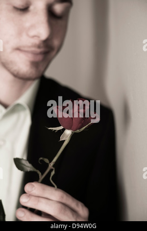 Close-up Portrait of Young Man holding Red Rose mit geschlossenen Augen, Studioaufnahme Stockfoto
