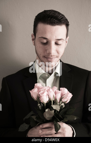 Porträt des jungen Mannes halten und auf der Suche nach unten in rosa Rosenstrauß, Studioaufnahme Stockfoto