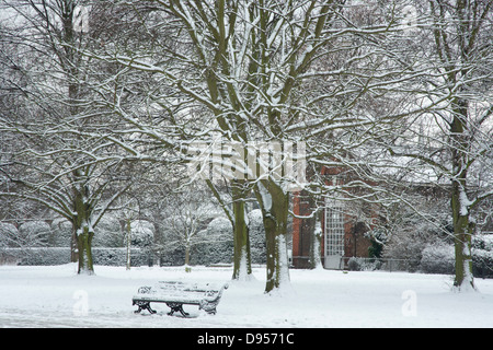 Eine verschneite Bank in den Kensington Gardens in der Nähe der Orangerie im Kensington Palace. London, UK Stockfoto