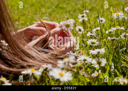 Junges Mädchen auf einem Rasen spielen mit Gänseblümchen und machen eine Daisy-Chain liegend Stockfoto