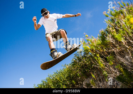 Niedrigen Winkel Blick auf eine Sandboarder springen über Dünenvegetation wolkenlosen blauen Himmel. Stockfoto