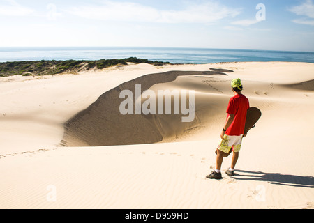 Rückansicht eines erwachsenen Mannes hält ein Sandboard und Blick auf das Meer auf den Dünen von Siriu Beach. Stockfoto