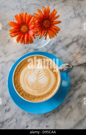 Eine Tasse Cappuccino mit einem ausgefallenen Design in die geschäumte Milch und eine Vase mit Blumen von oben gesehen. Stockfoto