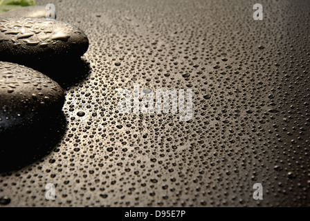 Massage-Steinen umgeben von Wassertropfen auf einem schwarzen Hintergrund Stockfoto