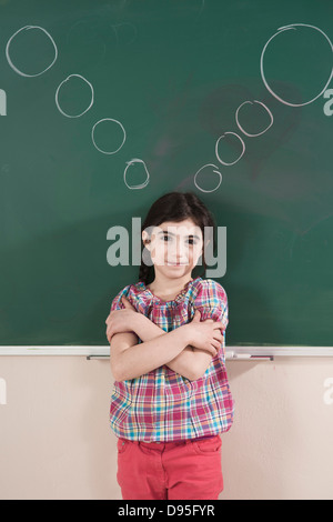 Mädchen vor der Tafel mit dachte Luftblasen im Klassenzimmer Stockfoto