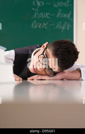 Junge mit Kopf auf den Schreibtisch vor Tafel im Klassenzimmer Stockfoto