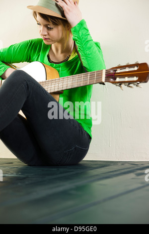 Porträt von Teenager Mädchen sitzen im Stock, trägt Hut und halten Akustikgitarre, Studioaufnahme auf weißem Hintergrund Stockfoto