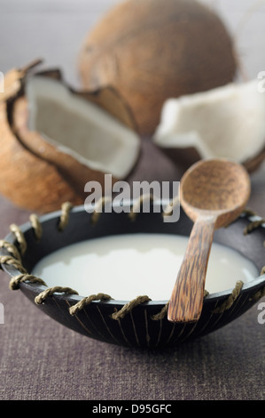 Kokos-Milch in Schüssel mit einem Holzlöffel, Kokosnüsse im Hintergrund Stockfoto