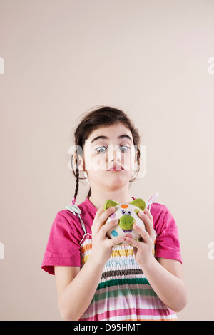 Porträt von Mädchen auf der Suche Cross Eyed Piggy Bank in Studio Stockfoto