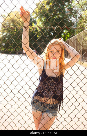 Porträt junge Frau stand hinter Maschendrahtzaun im Park in der Nähe Tennisplatz an warmen Sommertag in Portland Oregon USA Stockfoto