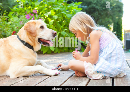 Kleines Mädchen malen die Krallen eines Hundes mit hell rosa Nagellack an einem sonnigen Sommernachmittag in Portland, Oregon, USA Stockfoto