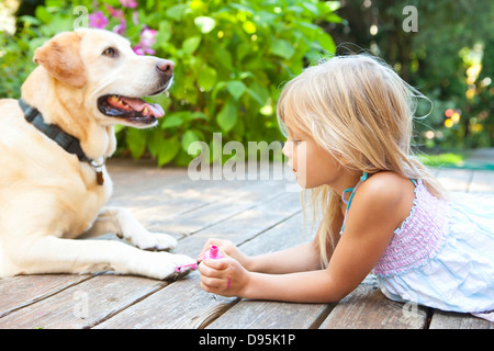 Kleines Mädchen malen die Krallen eines Hundes mit hell rosa Nagellack an einem sonnigen Sommernachmittag in Portland, Oregon, USA Stockfoto