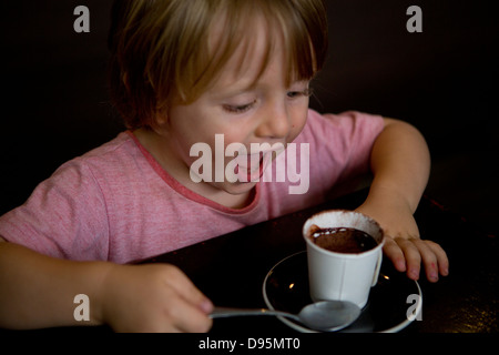 3 Jahre alter Junge Getränke warme Milch und Schokolade mit einem Löffel in einem café Stockfoto