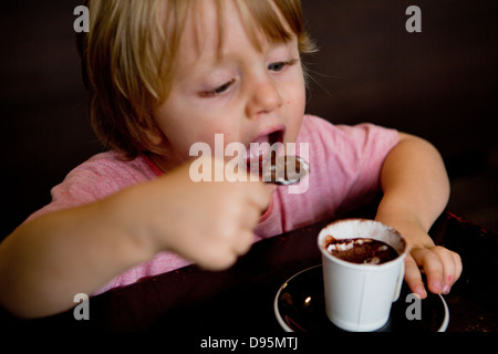 3 Jahre alter Junge Getränke warme Milch und Schokolade mit einem Löffel in einem café Stockfoto