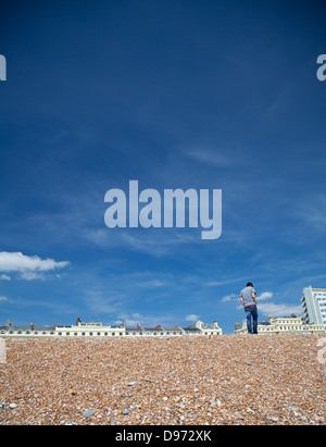 Eine einsame Figur / man zu Fuß am Strand von Brighton vor Botschaft Gericht mit blauem Himmel Stockfoto