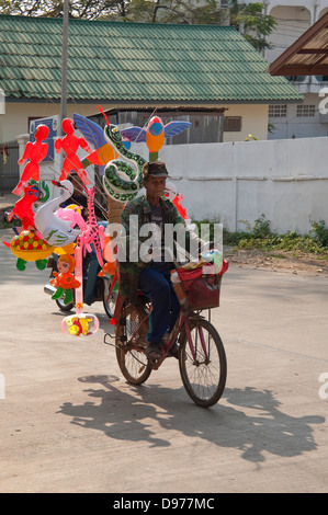 Vertikale Porträt eines alten laotischen Mannes, mit dem Fahrrad mit vielen verschiedenen geformten Ballons auf der Rückseite. Stockfoto