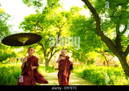 Zwei kleine buddhistische Mönche im freien laufen unter Schatten der grüne Baum vor Kloster, Myanmar. Stockfoto