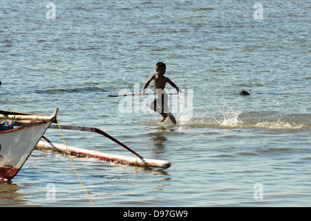 Ein Filipino junge zieht sich durch das seichte Wasser am Ufer des Bulalacao. Insel Mindoro, Philippinen Stockfoto