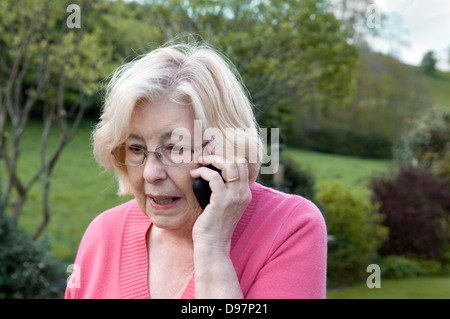 Ältere Dame mit Handy im Garten Stockfoto