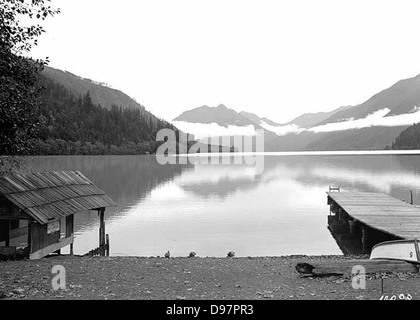 Ein abendlicher Blick auf Lake Crescent in Clallam County, Washington, mit ruhigem Wasser und Nebel. Das Foto fängt die ruhige Schönheit des Sees, der Olympic Mountains und der nahe gelegenen Bootshäuser ein. Stockfoto