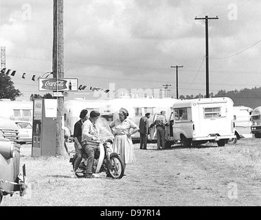 Bei der Airstream Rally treffen sich Menschen mit Anhängern und Coca-Cola-Maschinen. Es unterstreicht die Airstream-Kultur, die Reisetagebücher und ein Gefühl der Gemeinschaft unter Wohnwagen umfasst, oft begleitet von Vintage-Coca-Cola-Maschinen und Motorrädern. Stockfoto